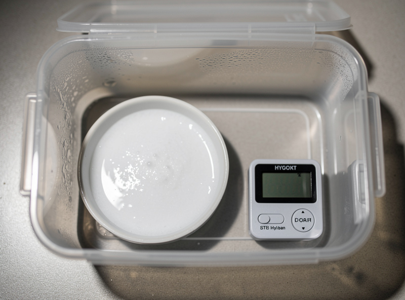 Salt slurry calibration setup with a small ceramic dish of wet salt next to a digital hygrometer reading 75 percent inside a sealed clear plastic container