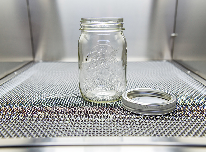 Macro photograph of a HEPA laminar flow hood with visible silver mesh filter face and an open mason jar in the working zone