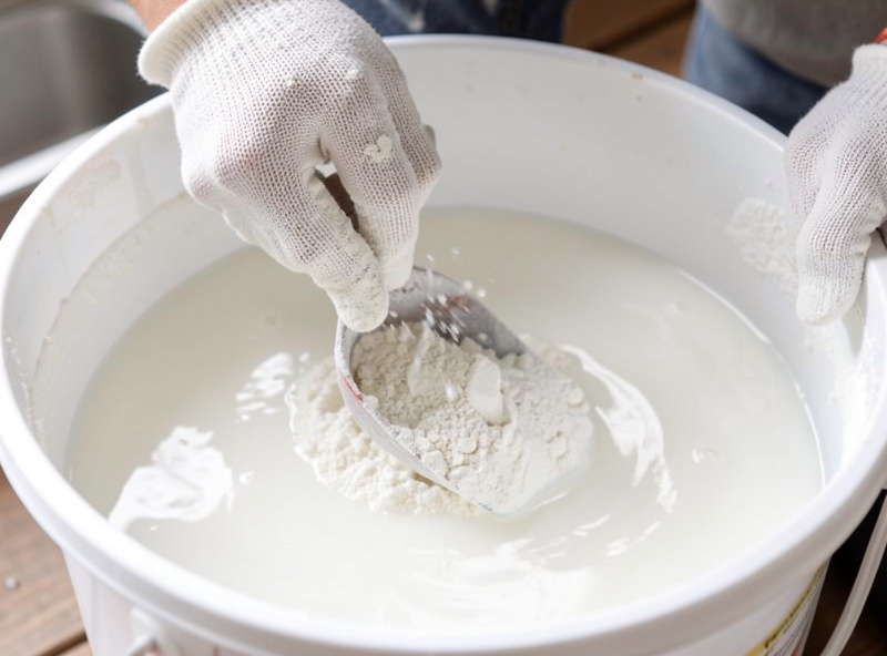 Gloved hands stirring hydrated lime powder into a bucket of water turning it cloudy white