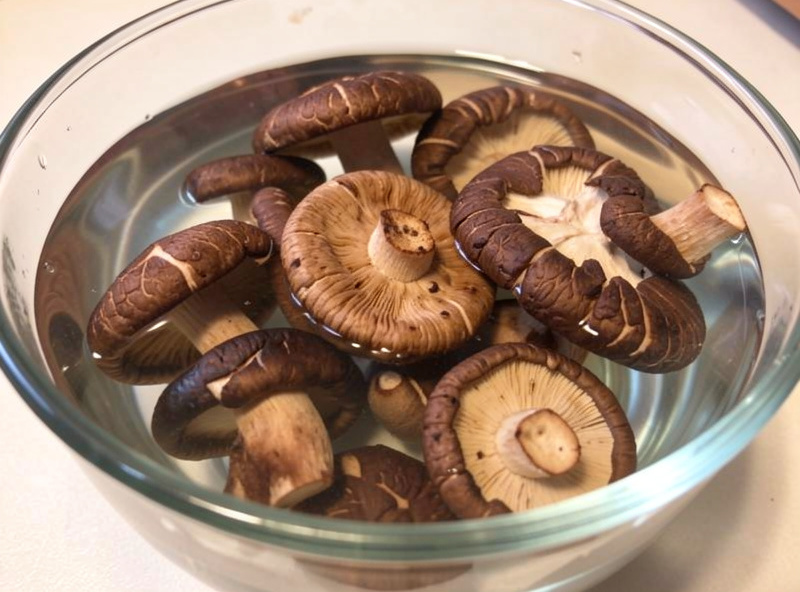 Dried shiitake and porcini mushrooms rehydrating in a clear glass bowl of water
