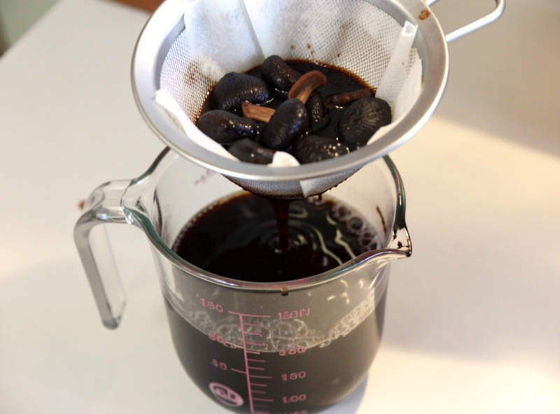 Dark mushroom soaking liquid being strained through a coffee filter into a measuring jug